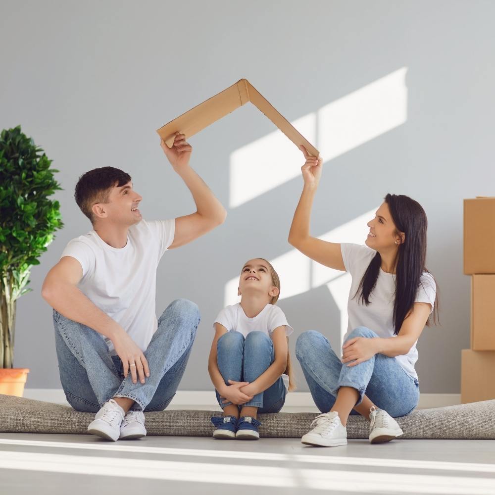 Family holding a cardboard house shape while sitting together at home